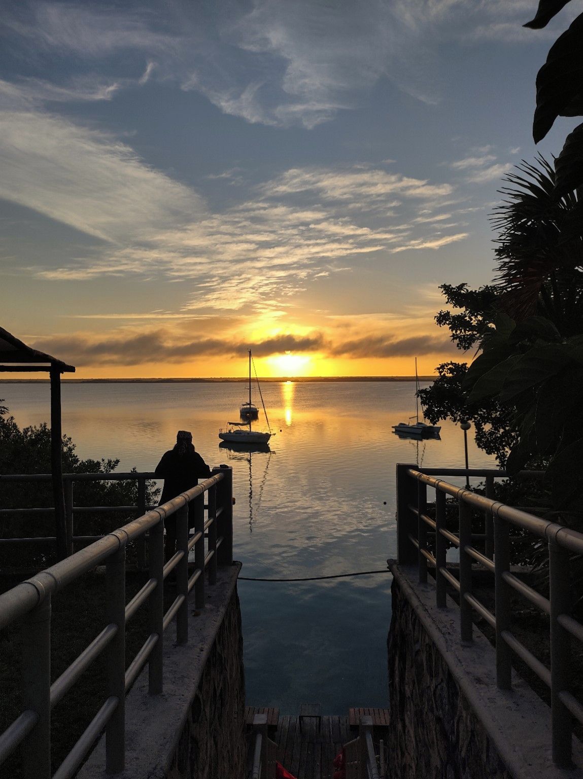Une vue sur le coucher de soleil depuis une jetée, avec des bateaux ancrés dans des eaux calmes.
