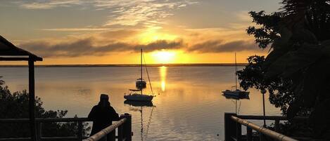 A sunset view from a pier with boats anchored in calm waters.