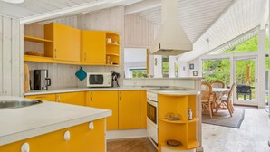 Una cocina con gabinetes amarillos, un microondas y una estufa. Hay una zona de comedor con una mesa y sillas.