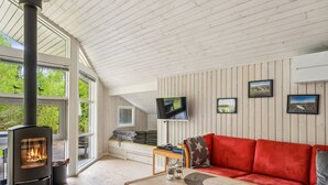 Una sala de estar acogedora con una estufa de leña, un sofá rojo, un televisor y cuadros en la pared.