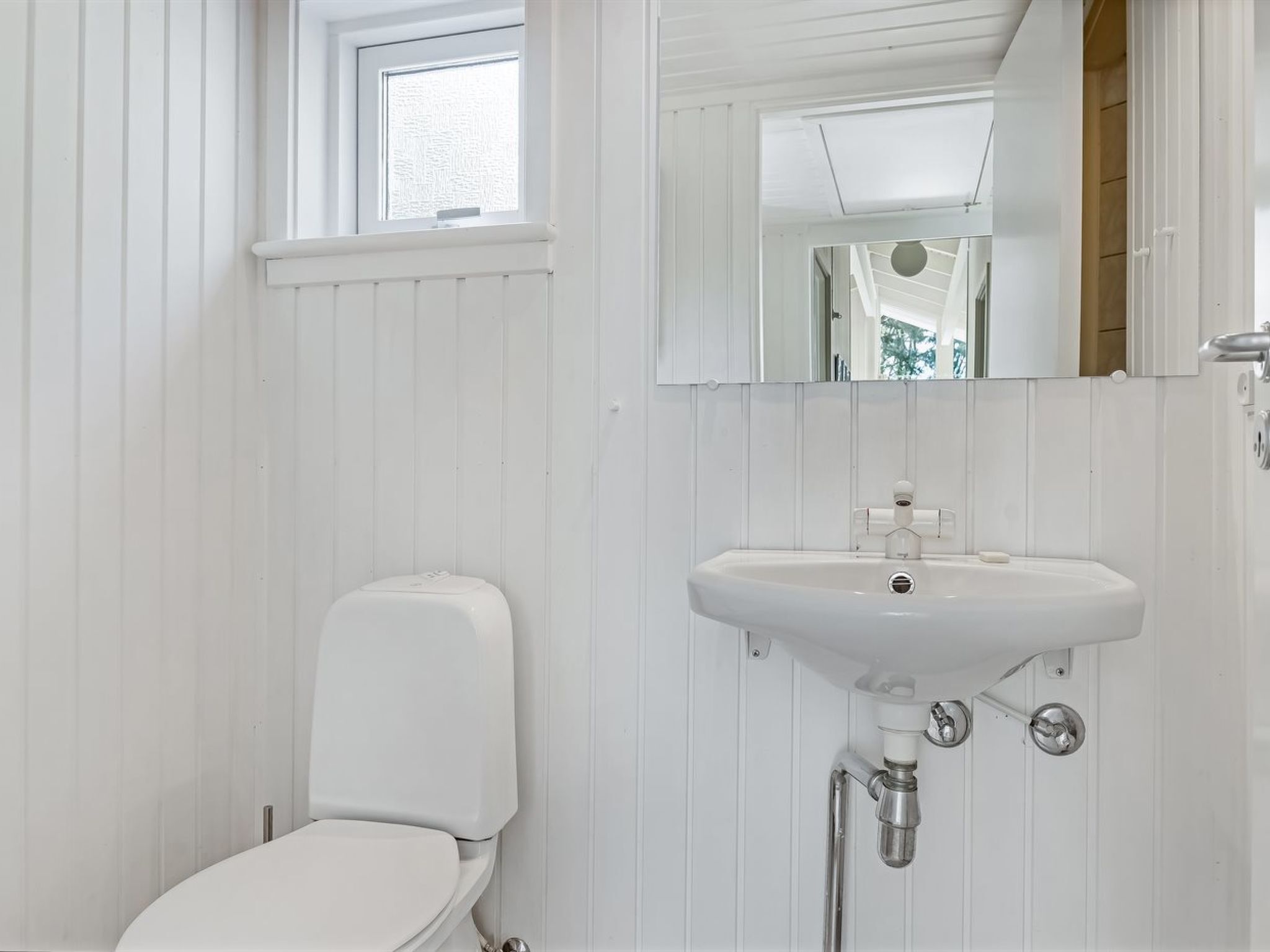 A bathroom with a white toilet, a sink with a mirror above it, and a window above the toilet.