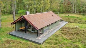 Rustiikkinen mökki, jossa on metallikatto, puinen terassi ja pieni kuisti.
