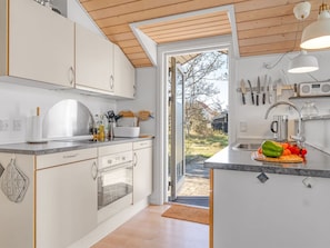 A modern kitchen with white cabinets, a built-in oven, a large window, and a wooden ceiling.