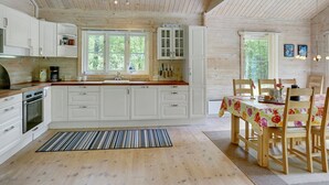 Een ruime keuken met witte kastjes, een houten aanrechtblad en een eethoek met een tafelkleed met bloemen.