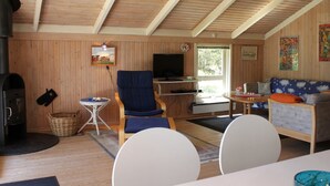 Interior acogedor de una cabaña con techo de madera, chimenea, televisor, sofá y mesa de comedor.