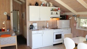Cocina compacta con muebles blancos, cafetera, microondas y estufa. Hay un comedor con mesa y sillas.