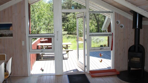 Una cabaña con techo a dos aguas, amplios puertas correderas de vidrio, una terraza de madera con mesas de picnic y un estufa de leña.