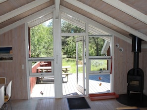 Une cabane avec un plafond mansardé, de grandes portes-fenêtres coulissantes, une terrasse en bois avec des tables de pique-nique et un poêle à bois.