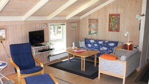 Una sala de estar acogedora con techo de madera, un televisor, un sofá con cojines estampados con motivos de nubes y una mesita con una bandera.
