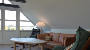 A cozy loft-style living room with a high ceiling, a large window, a leather sofa, a green armchair, and a small round table. - "Tara" - 300m from the sea by Interhome (Læsø)