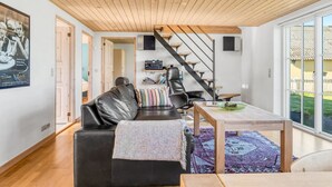 A modern living room with a black leather sofa, a wooden dining table, and a staircase leading to an upper level. - "Tara" - 300m from the sea by Interhome (Læsø)