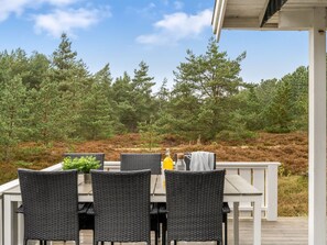 Ein Essbereich im Freien mit Korbstühlen und einem Tisch, umgeben von einer bewaldeten Landschaft.