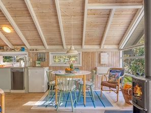 A cozy kitchen with wooden beams, a dining area with chairs, a table with a vase, and a wood-burning stove.