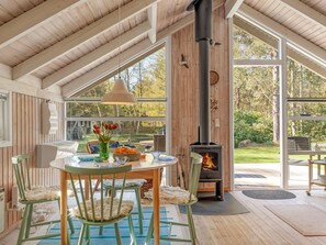 A cozy room with a wooden ceiling, a table with chairs, a vase of flowers, and a fireplace.