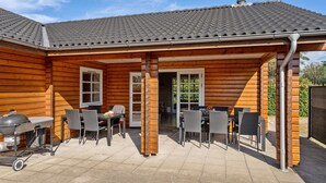 En træhytte med en terrasse, grill, spisebord og stole.