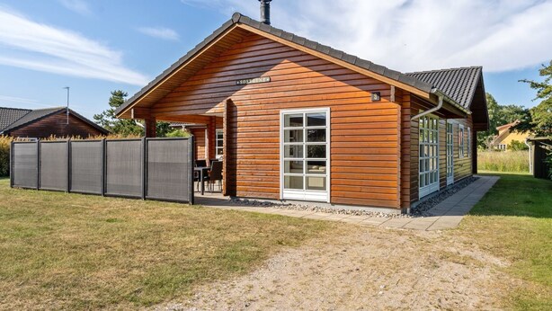 En træhytte med en overdækket terrasse, skorsten og en indhegnet have.