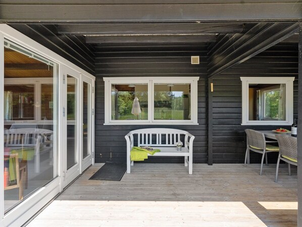 A covered porch with a white bench, two windows, and a table with chairs.