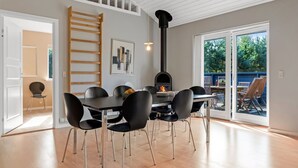 Un espace repas moderne avec une table et des chaises noires, une échelle en bois et une cheminée noire.