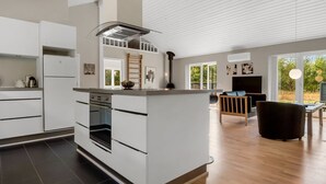Une cuisine moderne dotée d’un îlot central, d’un four encastré et d’une cuisinière. On y trouve également un coin repas avec un canapé et un téléviseur.