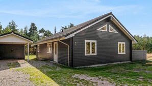 Une maison à deux étages, avec une façade sombre, des éléments décoratifs blancs et un toit en pente.