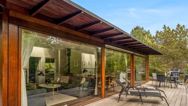 Una terrazza esterna moderna con una pergola, pareti in vetro e un'area pranzo con sedie e tavolo.