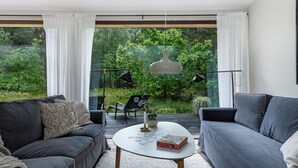 Un soggiorno moderno con due divani, un tavolino da caffè e vista su un giardino rigoglioso attraverso ampie finestre.