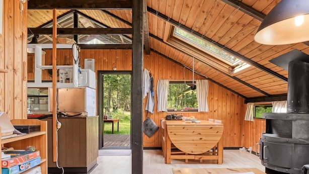 A cozy cabin interior with a wooden interior, a dining area, a kitchen with a stove, and a view of the outdoors.