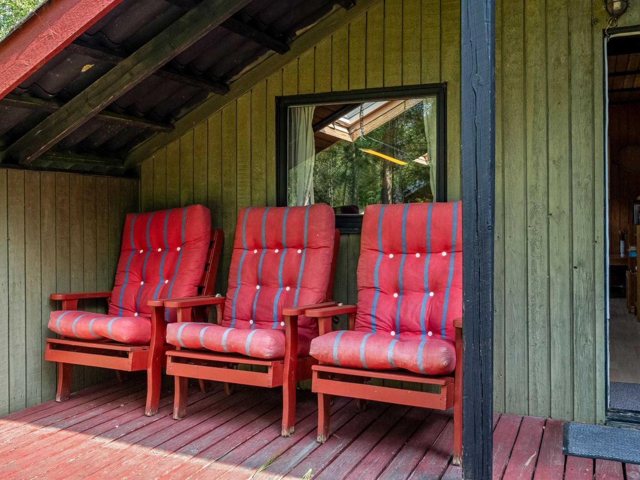 Une véranda avec trois chaises à l’assise rembourrée de tissu rouge et un banc en bois.