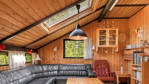 A cozy cabin interior with a leather sectional sofa, a wooden dining table, and a bookshelf.