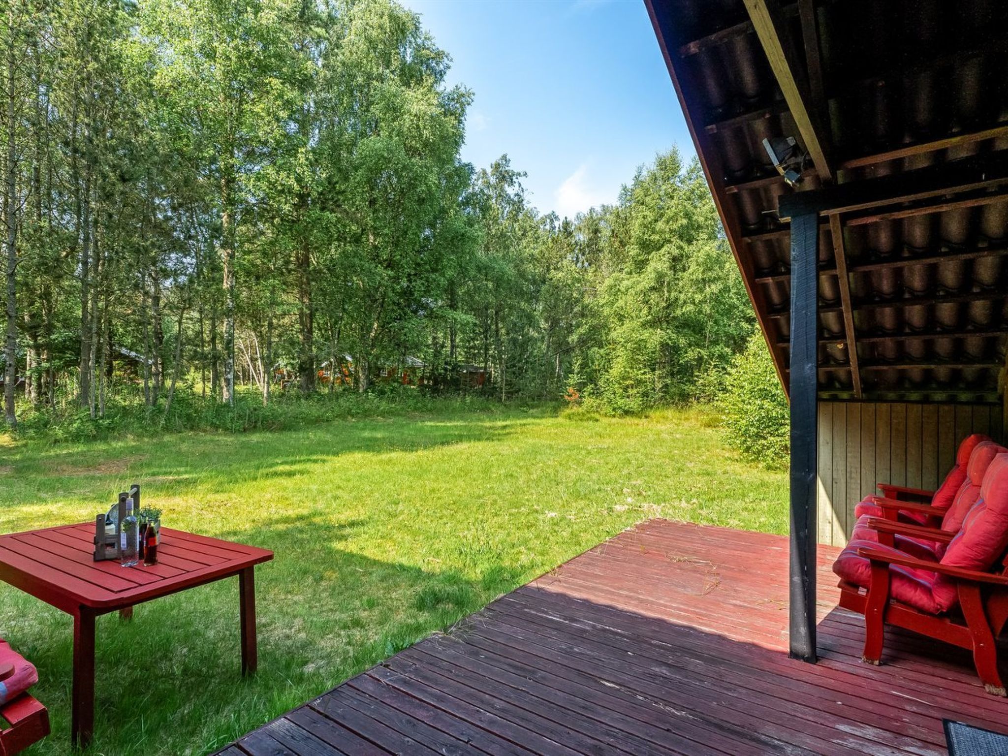 Een houten terras met een rode tafel en stoelen, met uitzicht op een grasveld met bomen.