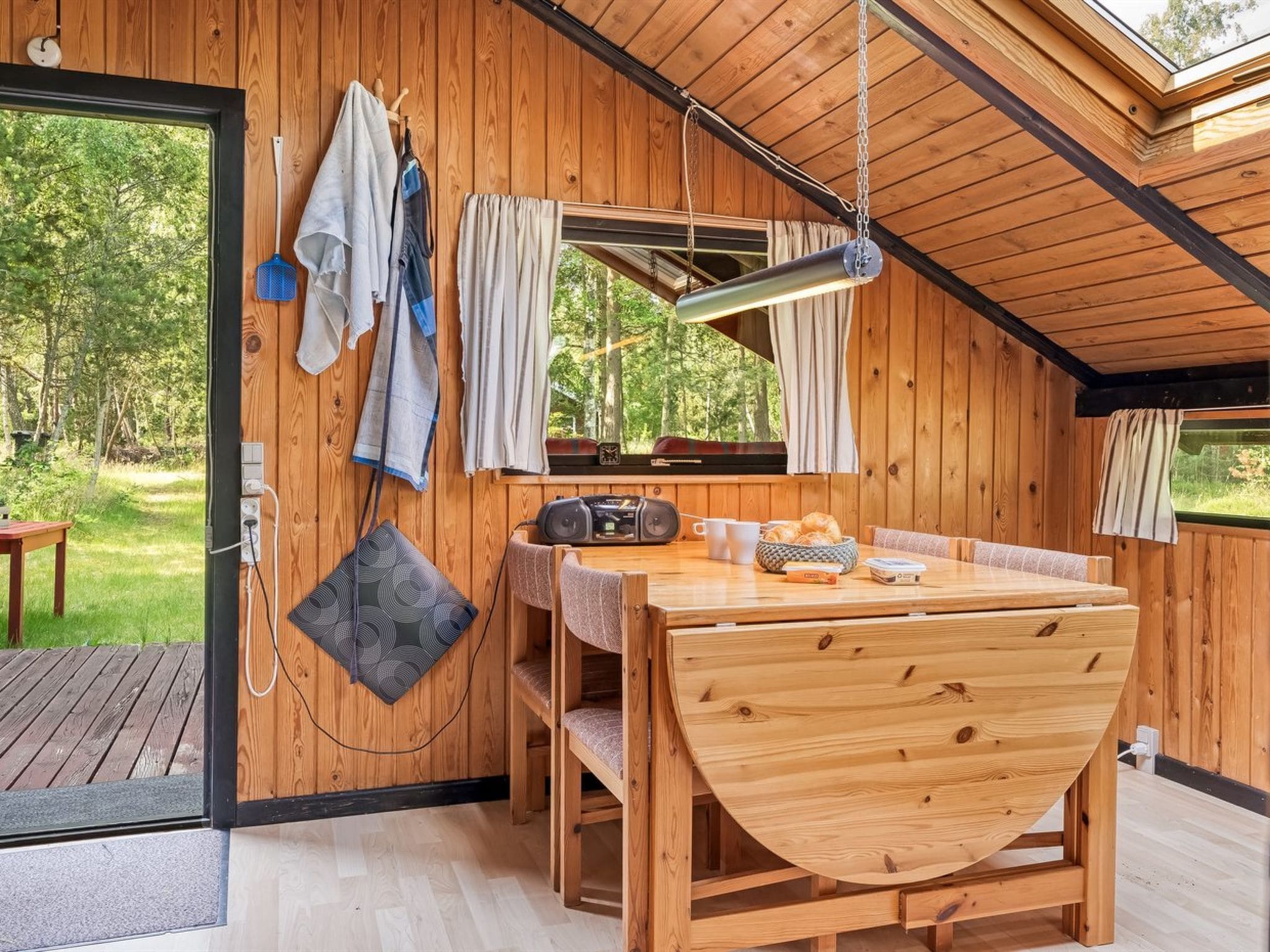 L’intérieur d’un chalet en bois chaleureux et accueillant, avec un coin repas, un téléviseur et une fenêtre donnant sur une forêt.