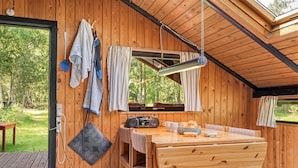 A cozy wooden cabin interior with a dining area, a TV, and a window overlooking a forest.