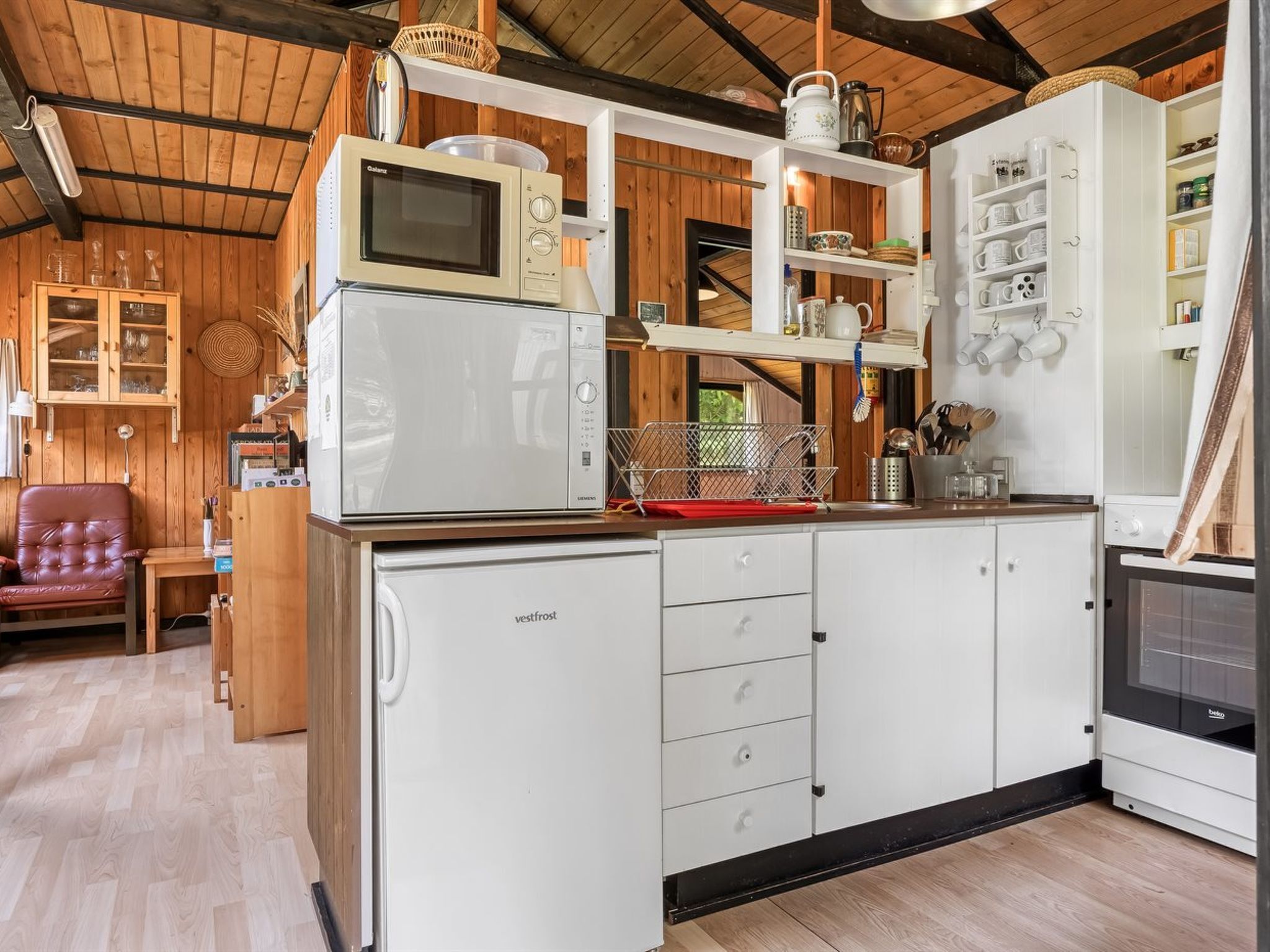 Una cocina compacta con microondas, refrigerador y pileta. Hay muebles de madera y una silla en la habitación.