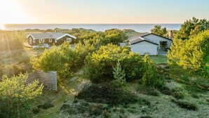 Ein Küsteneigentum mit zwei Hütten, eine mit Satteldach und die andere mit Flachdach, umgeben von dichter Vegetation und Blick aufs Meer.