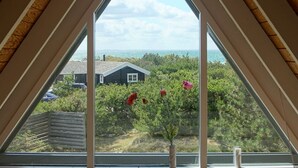 Ein dreieckiges Fenster mit Blick auf ein Haus, Bäume und den Ozean.