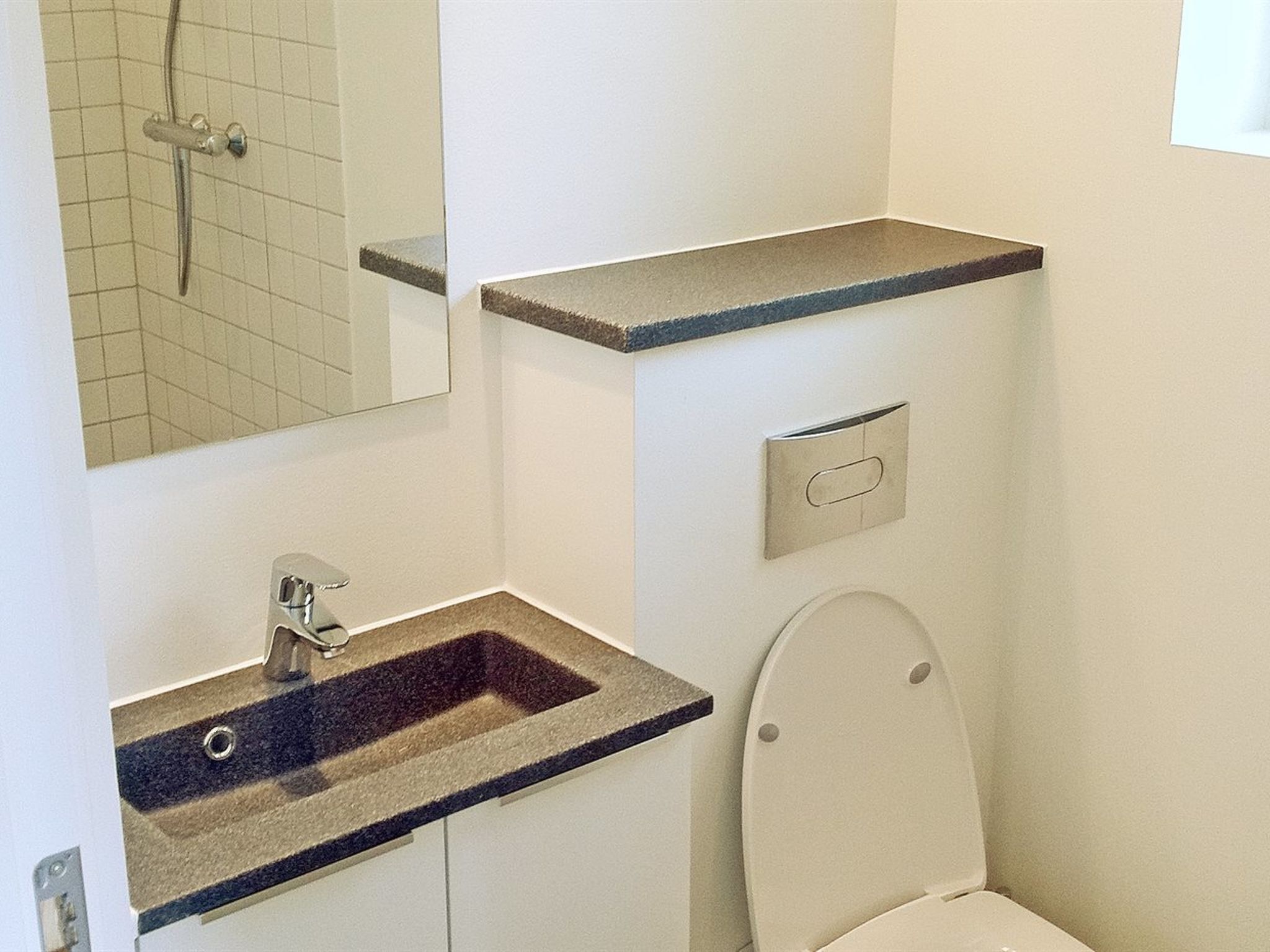 A bathroom with a sink, mirror, toilet, and a shower area.