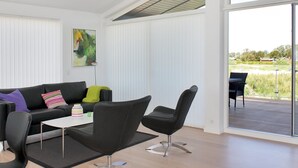 Un salon moderne comprenant un canapé, des fauteuils, une table basse et une grande fenêtre donnant sur un champ.
