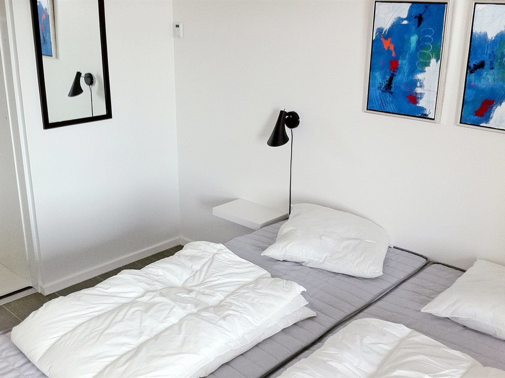 Een kamer met twee bedden, een nachtkastje, een lamp en abstracte schilderijen aan de muur.