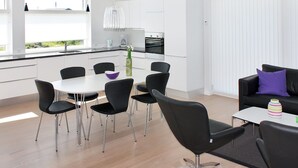 Une cuisine moderne avec des meubles blancs, un coin repas avec des chaises noires et un salon avec un canapé noir et une table basse.