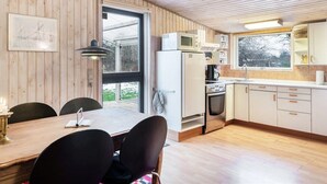 Una cocina moderna con paredes de madera, un área de comedor con mesa y sillas, y un ventanal que proporciona luz natural.