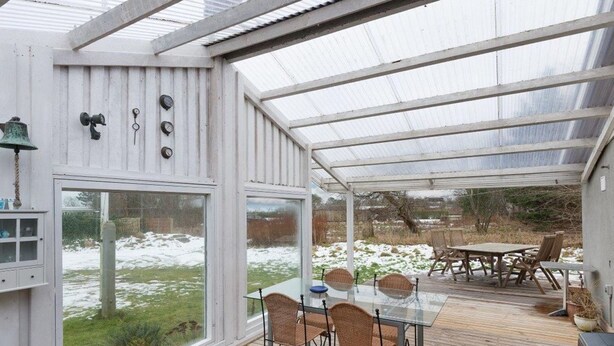 Un patio cubierto con una mesa y sillas de vidrio, una terraza de madera y vistas a un paisaje nevado.