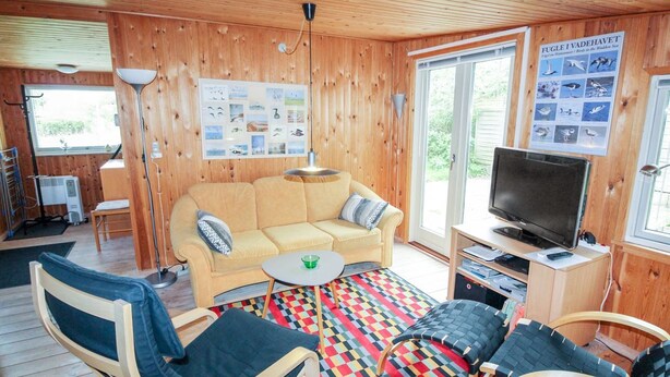 Interior acogedor de una cabaña con un sofá, dos sillones, un televisor y un cartel en la pared.