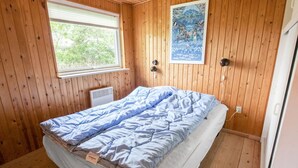 Habitación pequeña con una cama individual, paredes de madera y una ventana.