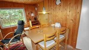 Interior de una cabaña de madera con una mesa de comedor, sillas, piso a cuadros, una ventana y un reloj en la pared.
