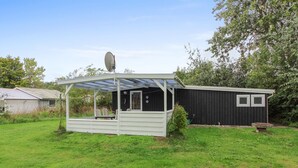 Un área de estar al aire libre techada con una mesa y sillas, una antena parabólica y un cobertizo en un patio cubierto de césped.