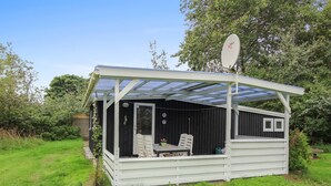 Una pequeña estructura exterior blanca, cubierta, con una mesa y sillas, rodeada de follaje.
