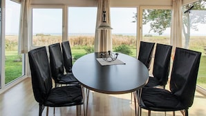 A round table with six black chairs, a pendant light, and a view of a grassy field through large windows.