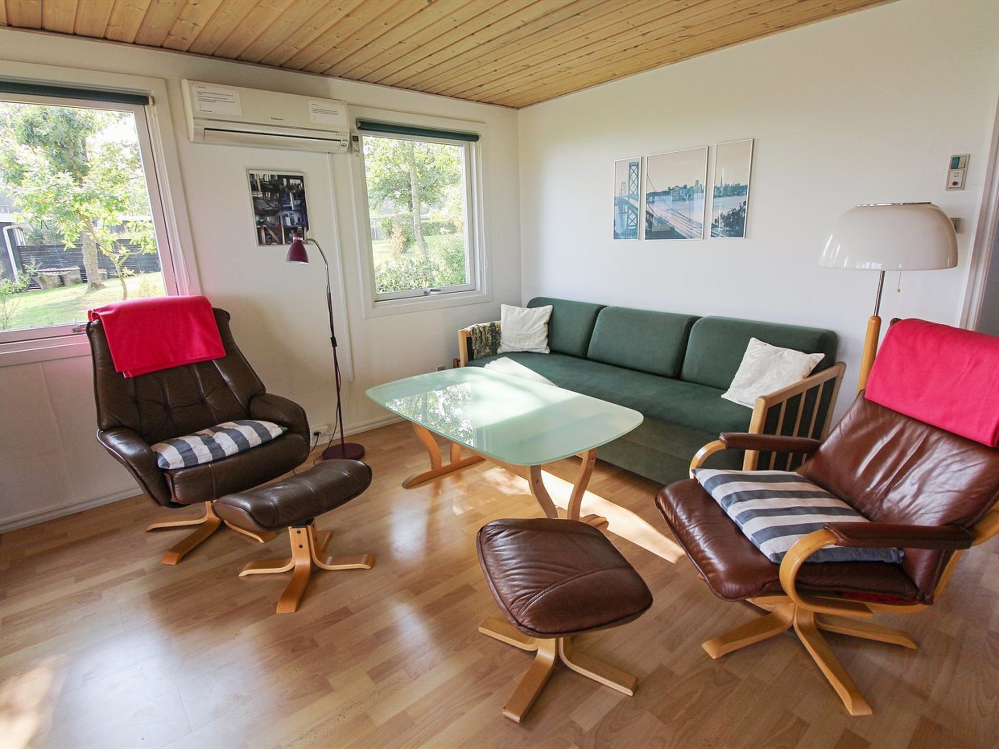 Un salon moderne avec un canapé vert, des fauteuils en cuir, une table basse en verre et un plaid rouge sur l’un des fauteuils.