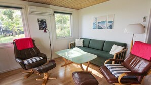 A modern living room with a green sofa, leather armchairs, a glass coffee table, and a red throw on one armchair.