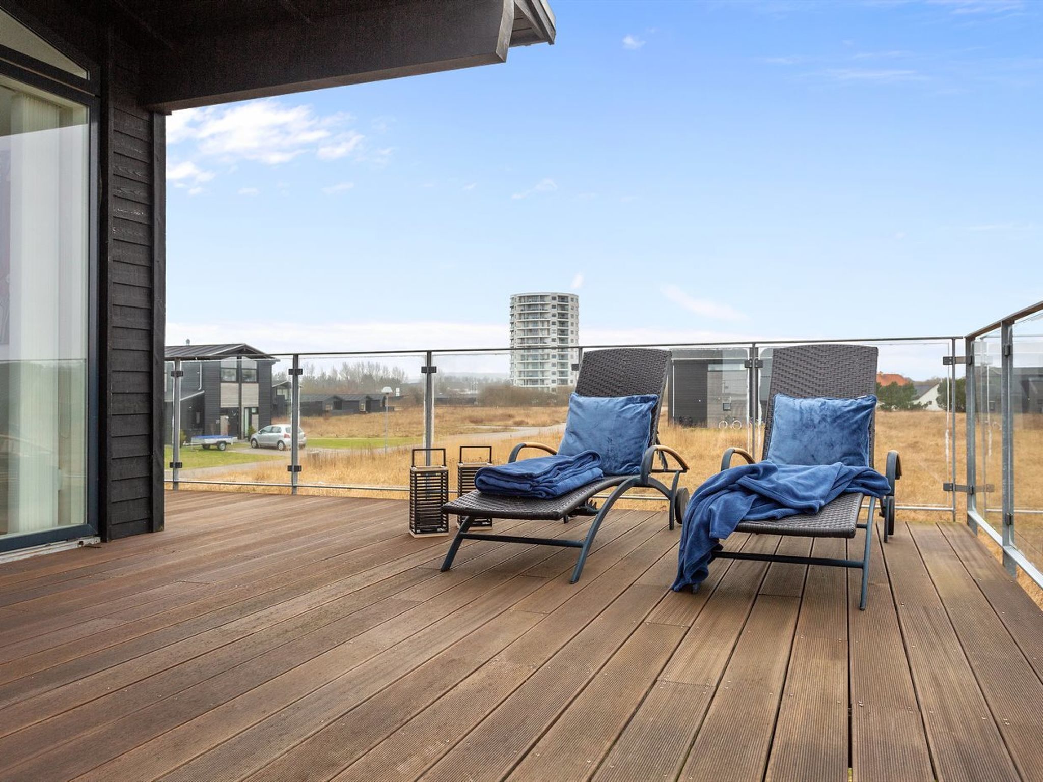 A balcony with two sun loungers, a wooden deck, and a view of a building and open field.